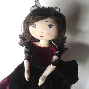 May include: A handmade doll with brown hair, wearing a black dress with lace sleeves and a burgundy velvet bodice.