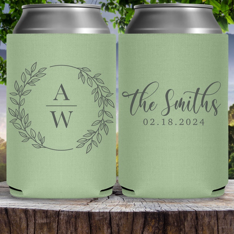 May include: Two green can coolers with a wedding theme. The cooler on the left has a wreath with leaves and the initials 'A W' inside. The cooler on the right has the text 'The Smiths' and the date '02.18.2024'.