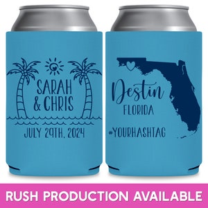 May include: Two blue and white can coolers. The left cooler has a palm tree design with the text 'Sarah & Chris' and 'July 29th, 2024'. The right cooler has a map of Florida with a heart over Destin, Florida. The text 'Destin Florida' and '#YourHashtag' are on the cooler.