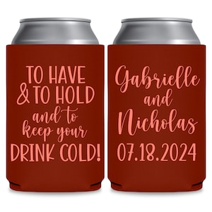 May include: Two red can coolers with white text. The left cooler says 'TO HAVE & TO HOLD and to keep your DRINK COLD!' The right cooler says 'Gabrielle and Nicholas 07.18.2024'.