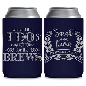 May include: Two navy blue can coolers with white text. The cooler on the left says 'we said the I DO'S now it's time for the BREWS'. The cooler on the right says 'Sarah and Kevin SEPTEMBER 27, 2024' with a wreath design around the names.