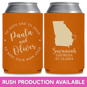 May include: Two orange can coolers with white text. The left cooler has the text 'To Have and To Hold Paula and Oliver To Keep Your Beer Cold'. The right cooler has the text 'Savannah Georgia 07.19.2024' and a white outline of the state of Georgia with a heart in the center.