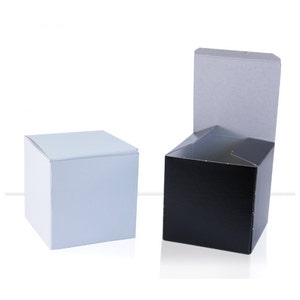 May include: Two square boxes, one white and one black. The black box is open with the lid folded back. Both boxes have a simple design.