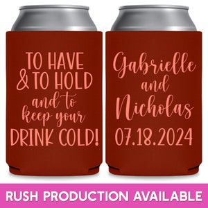 May include: Two red can coolers with white text. The left cooler says 'TO HAVE & TO HOLD and to keep your DRINK COLD!' The right cooler says 'Gabrielle and Nicholas 07.18.2024'.