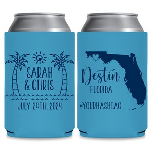May include: Two blue and white can coolers. The cooler on the left has a palm tree design, a sun, and the text 'Sarah & Chris' and 'July 29th, 2024'. The cooler on the right has an outline of the state of Florida with a heart over the state of Florida and the text 'Destin Florida' and '#YOURHASHTAG'.