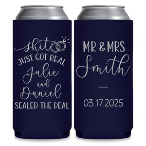 May include: Two navy blue can coolers with white text. The left cooler says 'Shit just got real Julie and Daniel Sealed the deal' with two silver rings and a diamond. The right cooler says 'Mr & Mrs Smith 03.17.2025'.