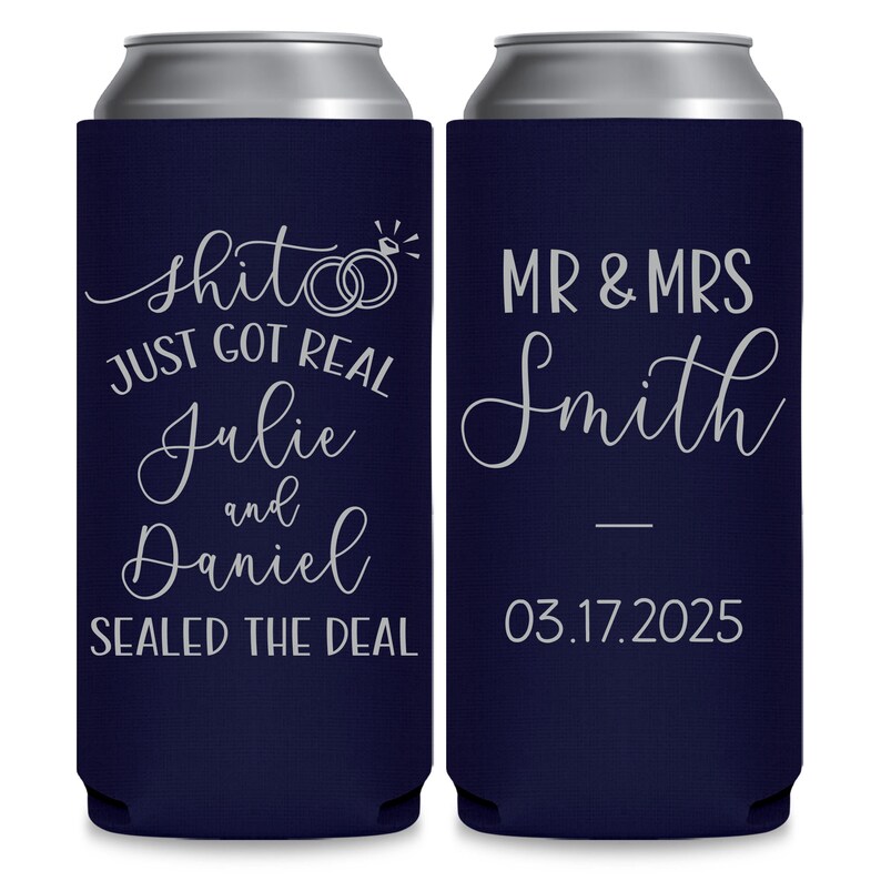 May include: Two navy blue can coolers with white text. The left cooler says 'Shit just got real Julie and Daniel Sealed the deal' with two silver rings and a diamond. The right cooler says 'Mr & Mrs Smith 03.17.2025'.