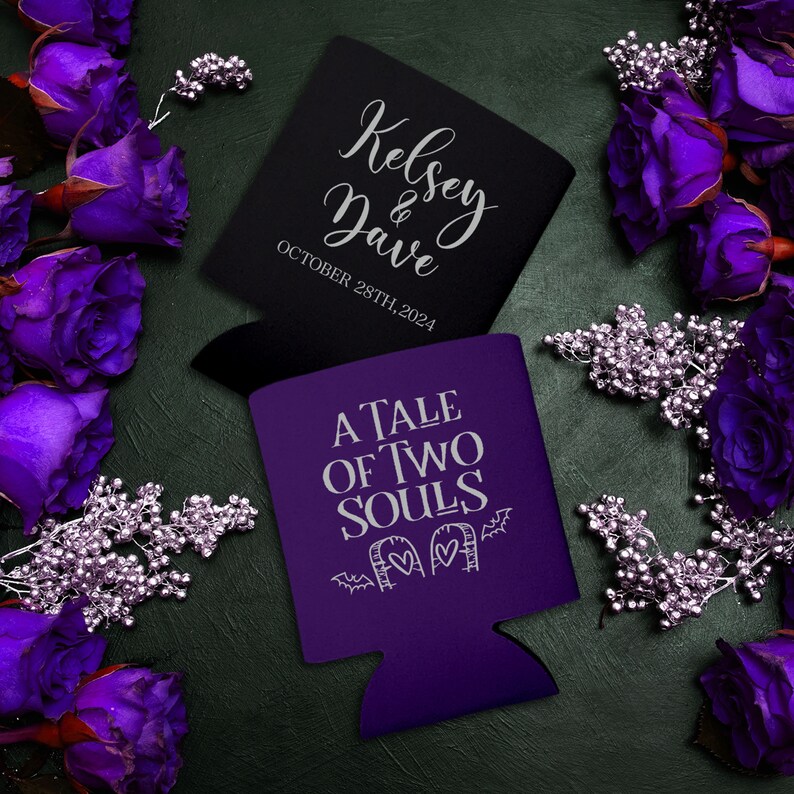 May include: Two purple and black can coolers. The purple cooler has the text 'A Tale of Two Souls' with a tombstone and bats. The black cooler has the text 'Kelsey & Dave' and 'October 28th, 2024'.