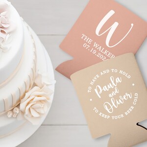 May include: Two personalized wedding can coolers. One is light pink with the letter 'W' and the text 'The Walker 07.19.202.' The other is beige with the text 'To have and to hold Paula and Oliver to keep your beer cold.' 