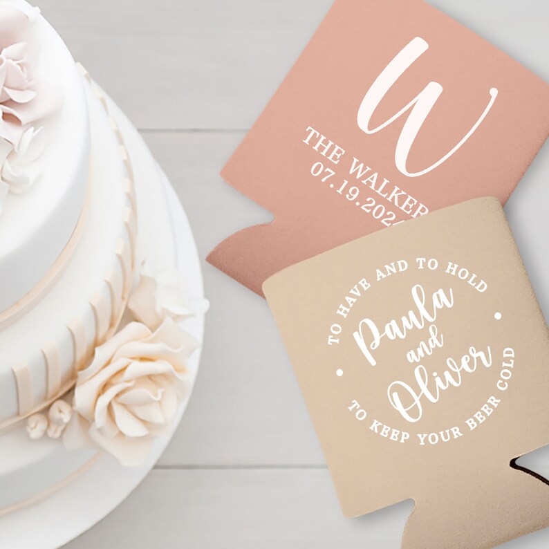 May include: Two personalized wedding can coolers. One is light pink with the letter 'W' and the text 'The Walker 07.19.202.' The other is beige with the text 'To have and to hold Paula and Oliver to keep your beer cold.' 