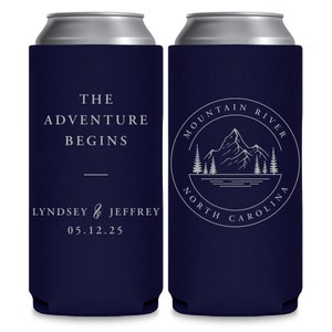 May include: Two navy blue can coolers with white text. The cooler on the left says 'The Adventure Begins' and 'Lyndsey & Jeffrey 05.12.25'. The cooler on the right has a circular design with a mountain, trees, and a river inside. The text around the design says 'Mountain River North Carolina'. 