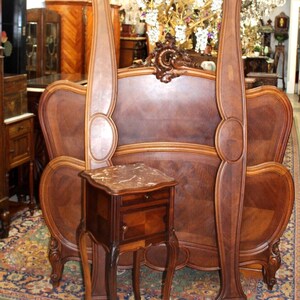 May include: A vintage wooden headboard with ornate carvings and a matching nightstand with a marble top. The headboard is made of dark wood and has a curved design. The nightstand is also made of dark wood and has a single drawer. The set is in good condition and would be a beautiful addition to any bedroom.
