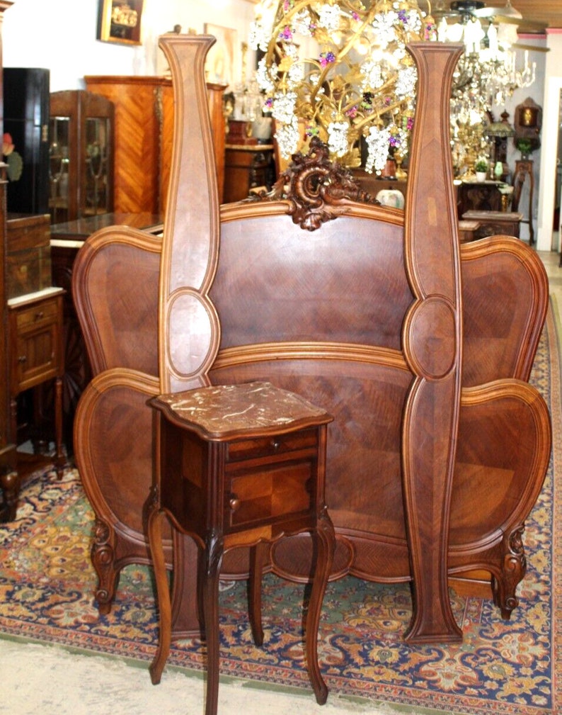 May include: A vintage wooden headboard with ornate carvings and a matching nightstand with a marble top. The headboard is made of dark wood and has a curved design. The nightstand is also made of dark wood and has a single drawer. The set is in good condition and would be a beautiful addition to any bedroom.