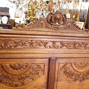 May include: A large, intricately carved wooden cabinet with two doors. The cabinet is made of dark wood and features a decorative top with a floral design. The doors are also carved with floral designs.