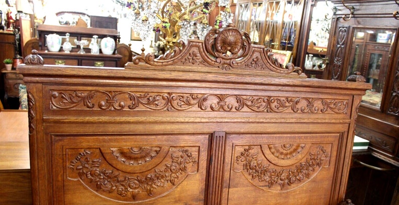 May include: A large, intricately carved wooden cabinet with two doors. The cabinet is made of dark wood and features a decorative top with a floral design. The doors are also carved with floral designs.