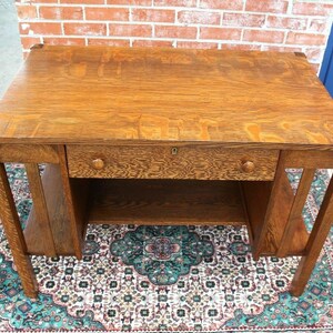 May include: A vintage wooden desk with a single drawer and a lower shelf. The desk is made of dark wood with a natural finish. The desk is sitting on a patterned rug.