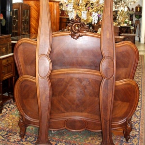 May include: A wooden headboard with ornate carvings and a curved design. The headboard is made of dark wood with a rich grain pattern. The headboard is in a vintage style and would be a beautiful addition to any bedroom.