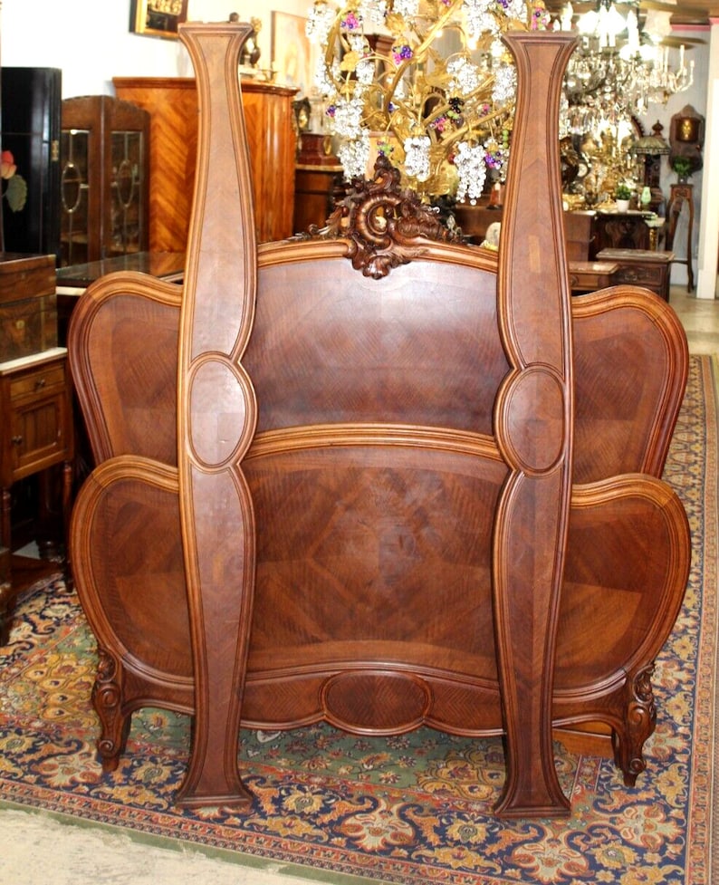 May include: A wooden headboard with ornate carvings and a curved design. The headboard is made of dark wood with a rich grain pattern. The headboard is in a vintage style and would be a beautiful addition to any bedroom.