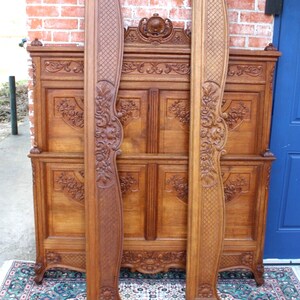 May include: A carved wooden headboard featuring intricate floral and scrollwork designs. The headboard is crafted from oak and has a rich brown colour. The headboard is in good condition and displays a classic French style.