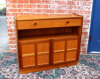 May include: A mid-century modern teak wood cabinet with two drawers, a shelf, and two doors. The doors have a geometric pattern and the cabinet has a warm brown finish.