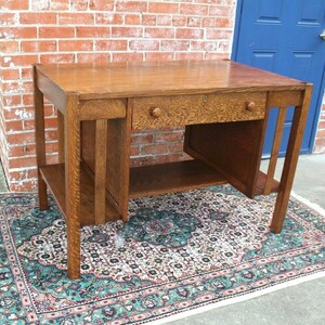 May include: A vintage oak desk with a single drawer and a lower shelf. The desk has a simple, elegant design with clean lines and a rich wood finish.