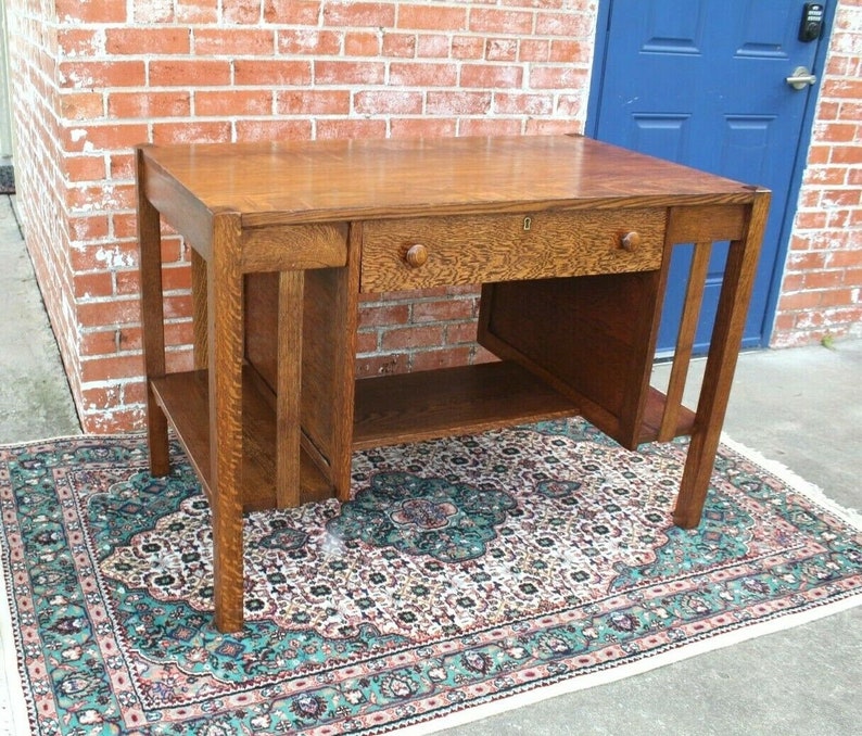 May include: A vintage oak desk with a single drawer and a lower shelf. The desk has a simple, elegant design with clean lines and a rich wood finish.