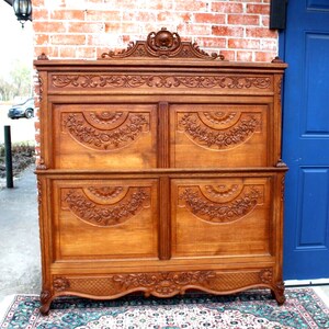 May include: A large, intricately carved wooden headboard with a floral design. The headboard is made of light brown wood and has a raised, ornate top.