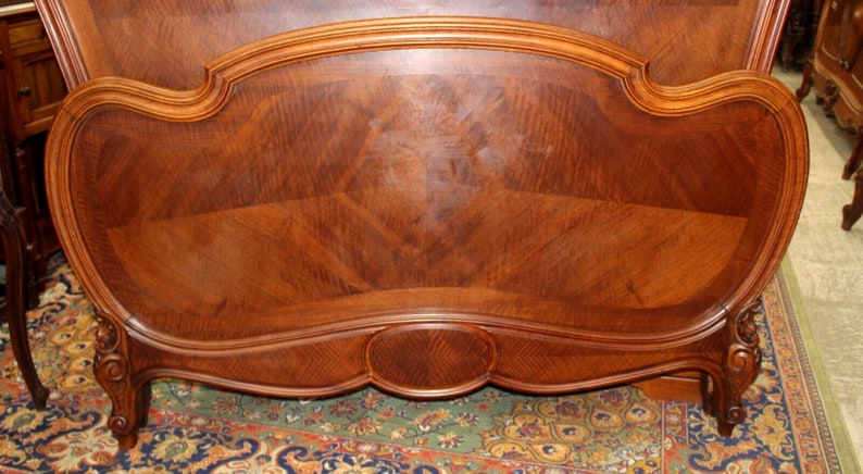 May include: A wooden headboard with a curved top and intricate carvings. The headboard is made of dark wood with a rich grain pattern.