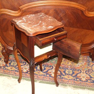 May include: A small, antique, wooden nightstand with a marble top and a single drawer. The drawer is open and the nightstand is sitting on a patterned rug.