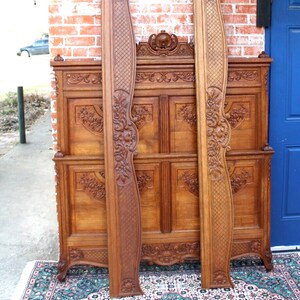 May include: A vintage wooden bed frame with intricate carvings and a headboard featuring a floral design. The frame is made of dark wood and has a distressed finish. The bed frame is standing on a patterned rug.
