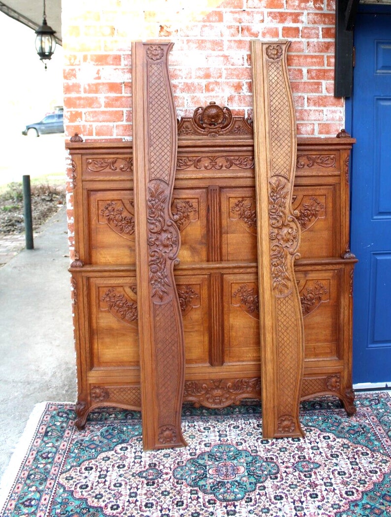 May include: A vintage wooden bed frame with intricate carvings and a headboard featuring a floral design. The frame is made of dark wood and has a distressed finish. The bed frame is standing on a patterned rug.