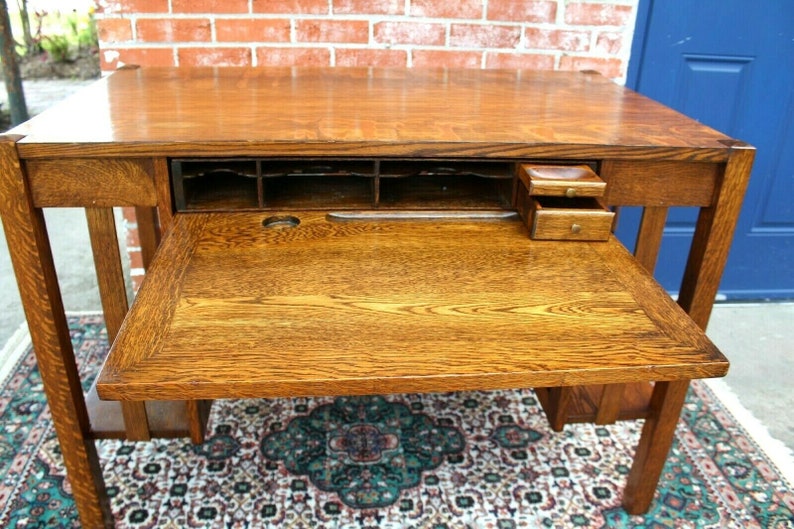 May include: A vintage wooden desk with a drop-down drawer and a small drawer on the right side. The desk has a dark wood finish and is in good condition.