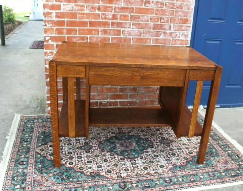 May include: A vintage wooden desk with a single drawer and a lower shelf. The desk is made of dark wood with a natural finish. It has a simple, rectangular design with straight lines and a slightly distressed look.