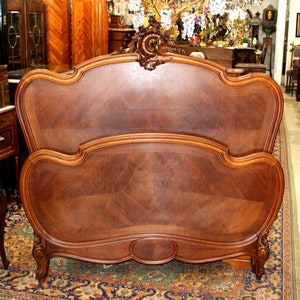 May include: A vintage wooden bed frame with a carved headboard and footboard. The frame is made of dark wood with a rich grain pattern. The headboard is curved and features a decorative design. The footboard is also curved and has a simple design.