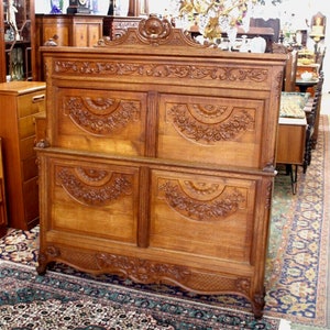 May include: A large, intricately carved wooden headboard with a decorative top and four panels. The headboard is made of light brown wood and features floral and scrollwork designs.