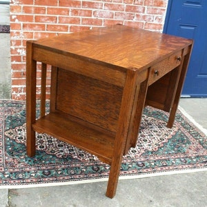 May include: A vintage wooden desk with a dark brown finish. The desk has a single drawer on the right side and a shelf below the desktop. The desk is sitting on a patterned rug.