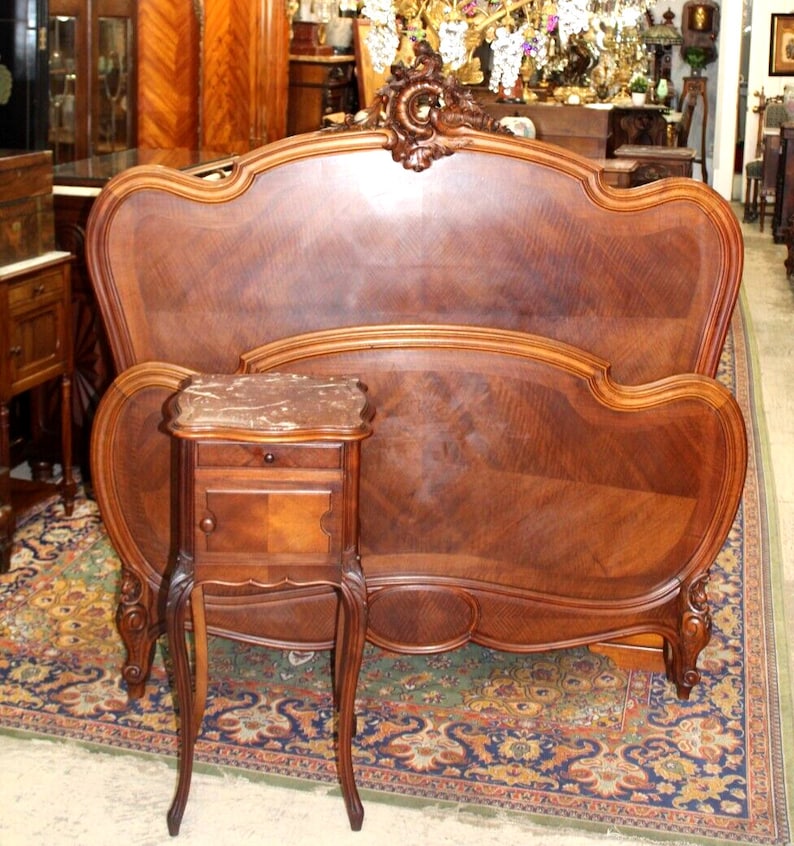 May include: A carved wooden headboard with a curved design and a matching nightstand with a marble top. The headboard and nightstand are both in a rich brown color.