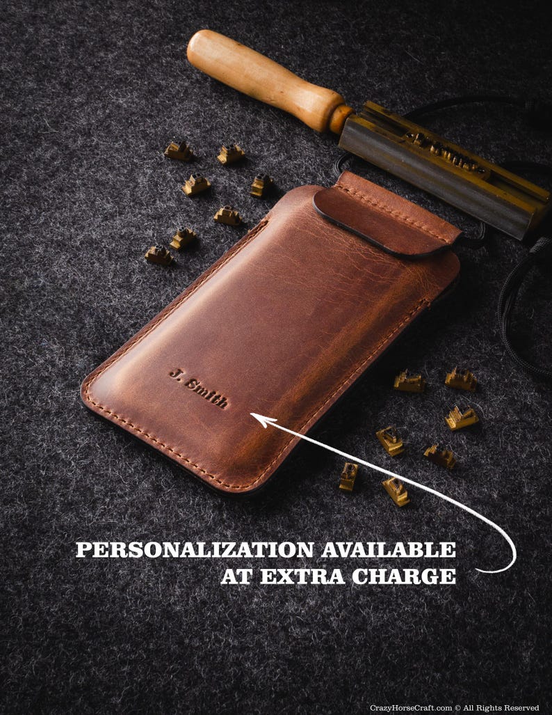 May include: A brown leather phone case with a flap closure. The case is personalized with the name "J. Smith". A metal tool and letter stamps are visible in the background.  Personalization is available at an extra charge.