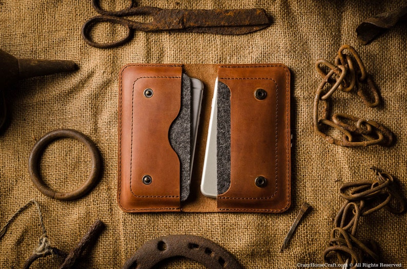 May include: A brown leather phone case with two pockets for cards and a flap to hold a phone. The case has a gray felt lining and is closed with a snap.