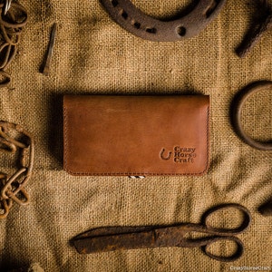 May include: A brown leather wallet with the text "Crazy Horse Craft" embossed on the front. The wallet is lying on a burlap surface with various metal objects around it.