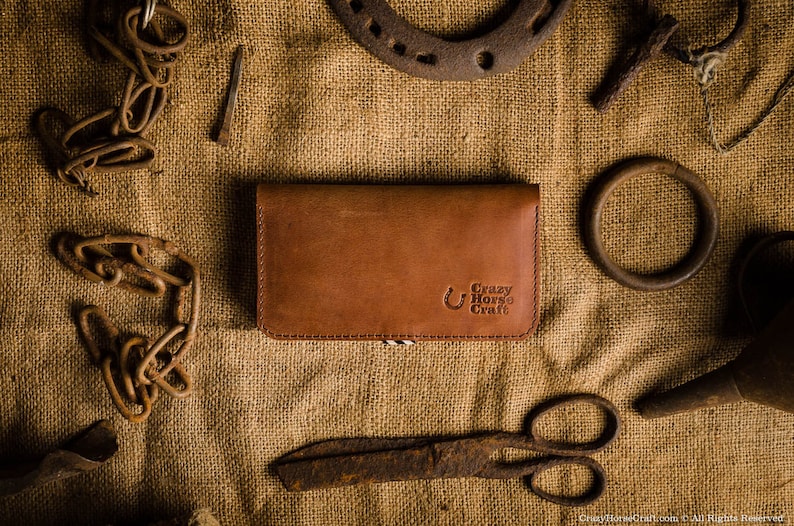 May include: A brown leather wallet with the text "Crazy Horse Craft" embossed on the front. The wallet is lying on a burlap surface with various metal objects around it.