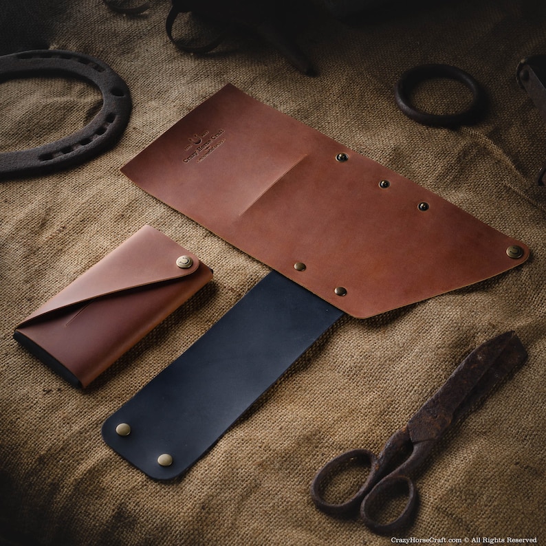 May include: A set of three brown leather wallets with a black leather strap. The wallets have a distressed look and are decorated with brass rivets. The wallets are arranged on a burlap background.