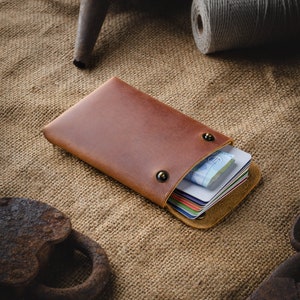 May include: A brown leather wallet with a flap closure and two brass snaps. The wallet is open and filled with credit cards and cash.