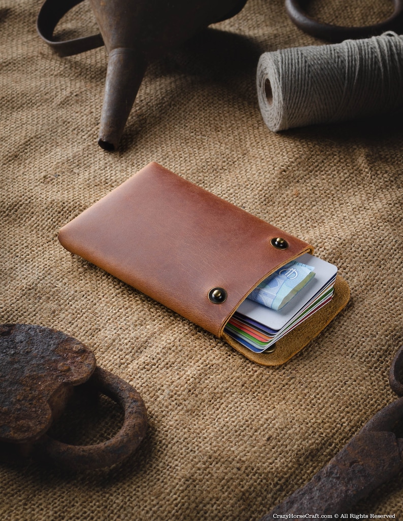 May include: A brown leather wallet with a flap closure and two brass snaps. The wallet is open and filled with credit cards and cash.