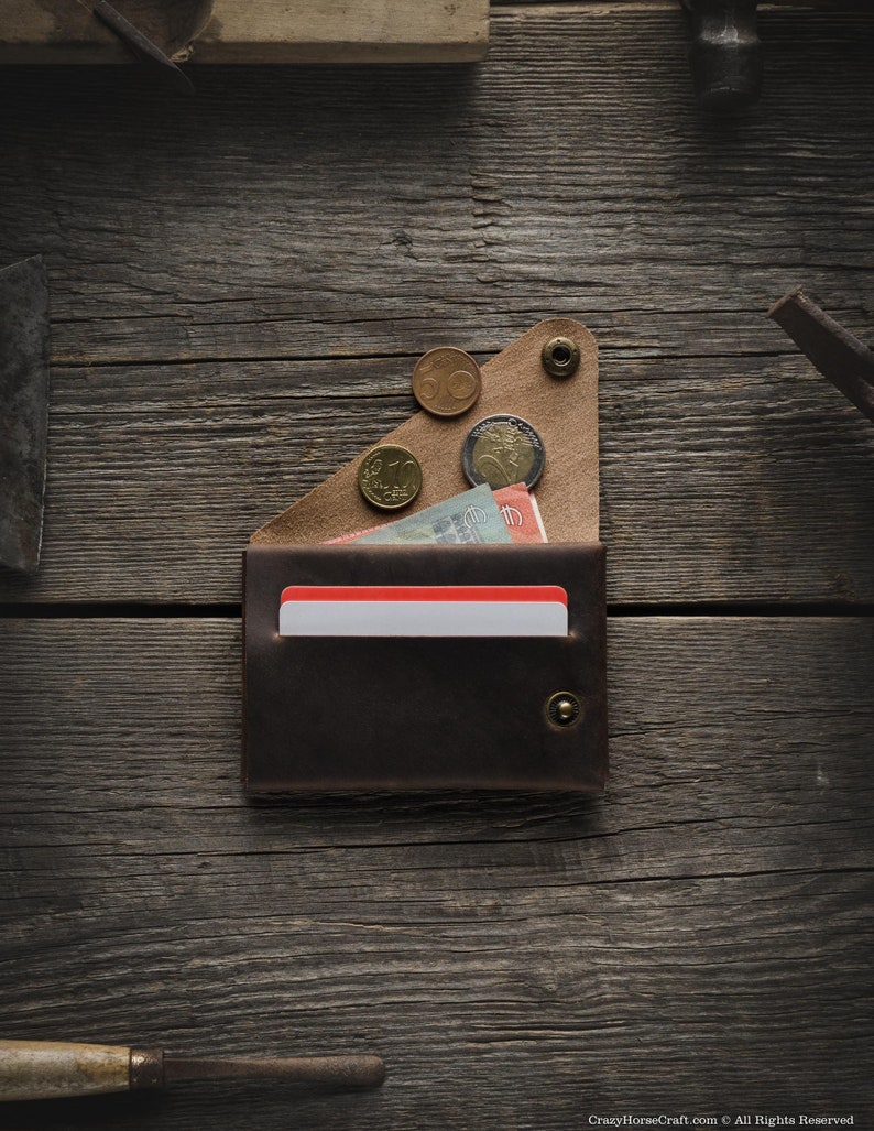 May include: A brown leather wallet with a red card holder and a flap that holds coins. The wallet is on a wooden surface.