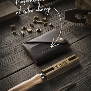 May include: A brown leather wallet with a personalized inscription "J. Smith" and a brass button. The wallet is on a wooden surface with a set of brass letter stamps and a wooden mallet.