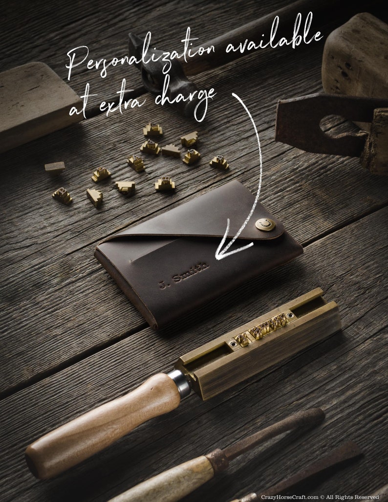 May include: A brown leather wallet with a personalized inscription "J. Smith" and a brass button. The wallet is on a wooden surface with a set of brass letter stamps and a wooden mallet.