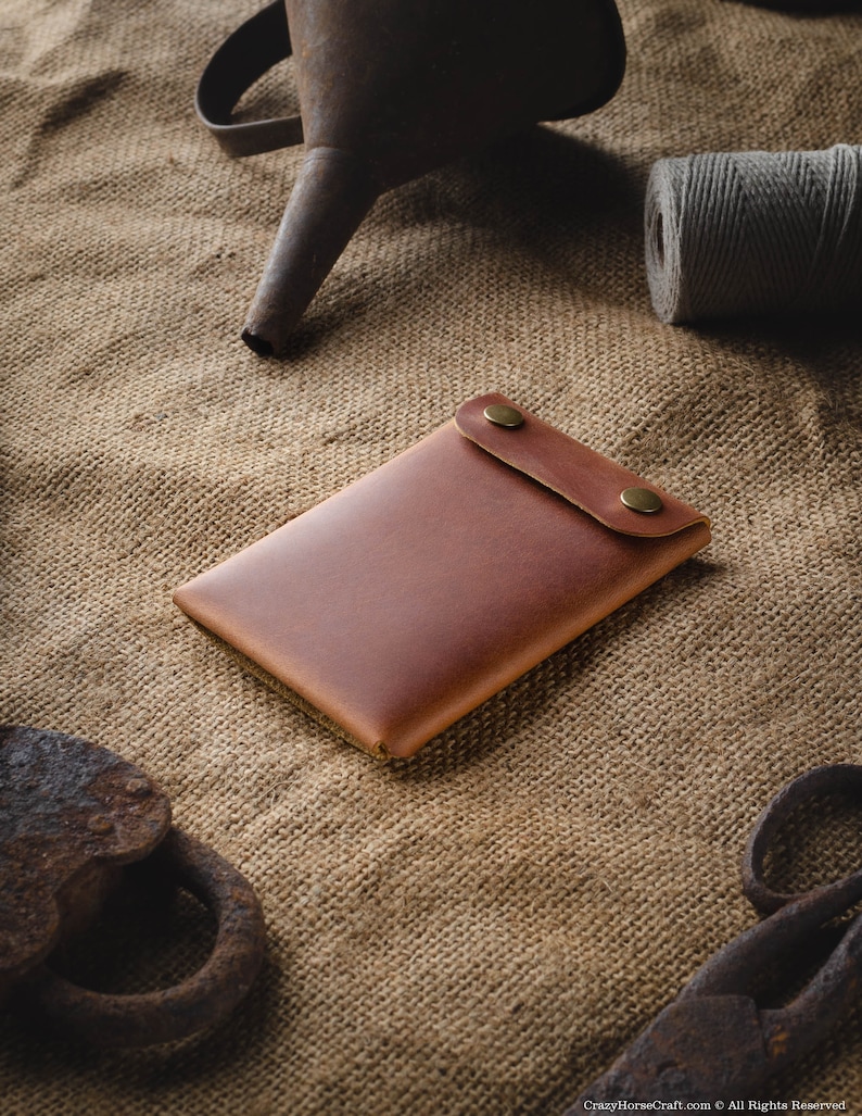 May include: A brown leather wallet with two brass snaps on a burlap background.
