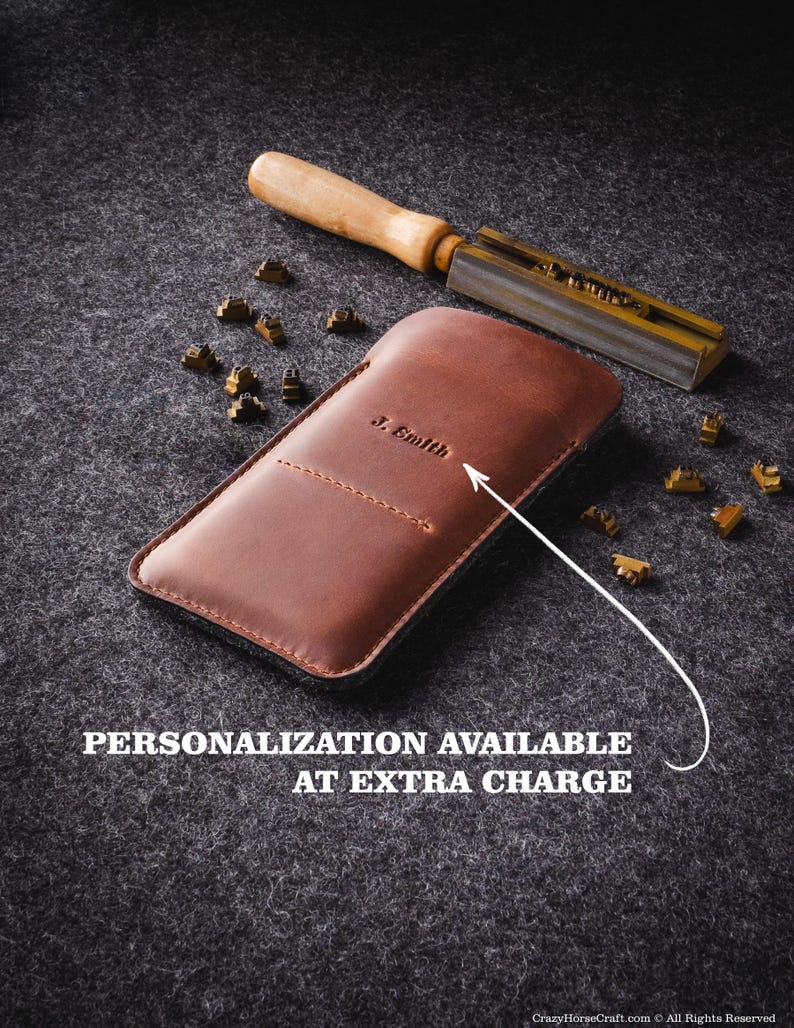 May include: A brown leather phone case with the name "J. Smith" embossed on the front. The case is lying on a gray surface with a metal tool and brass letters scattered around it. The text "PERSONALIZATION AVAILABLE AT EXTRA CHARGE" is printed below the case.