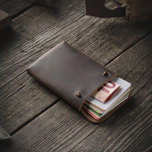 May include: A brown leather wallet with a stack of credit cards and a ten euro bill inside. The wallet is on a wooden surface.